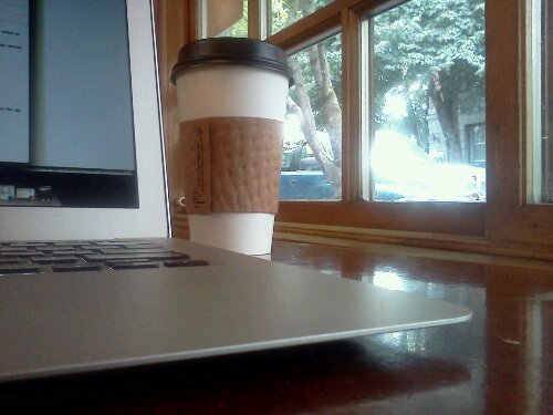 A coffee cup next to a laptop on a table.